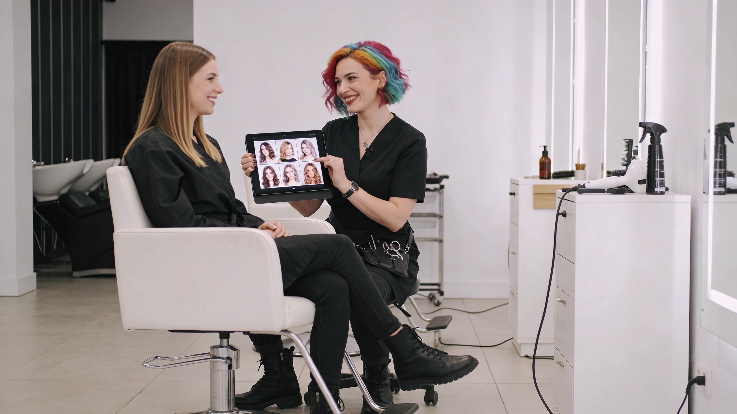 Coiffeuse montrant à une cliente un portfolio numérique de coiffures sur une tablette dans un salon moderne, les deux femmes souriantes et engageantes, lumière douce et professionnelle, style photo éditorial magazine