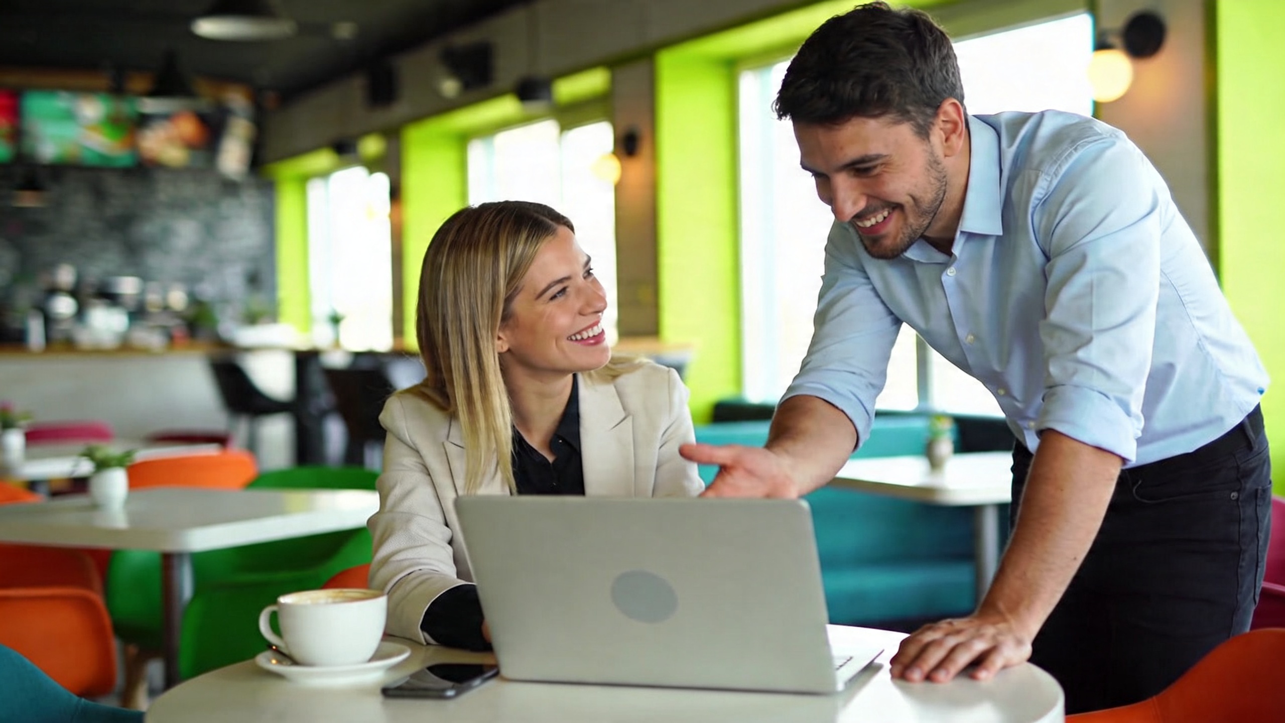 Coach femme et homme travaillant ensemble sur un projet, souriants et engagés, dans un café moderne et lumineux, style photo réaliste, composition dynamique, couleurs vives et ambiance collaborative